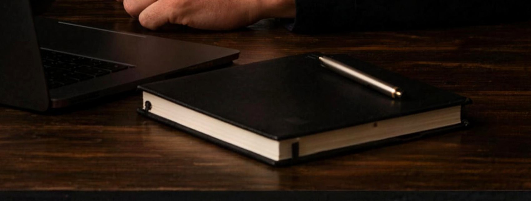 Werkbank: laptop, notitieboek en pen op donker hout